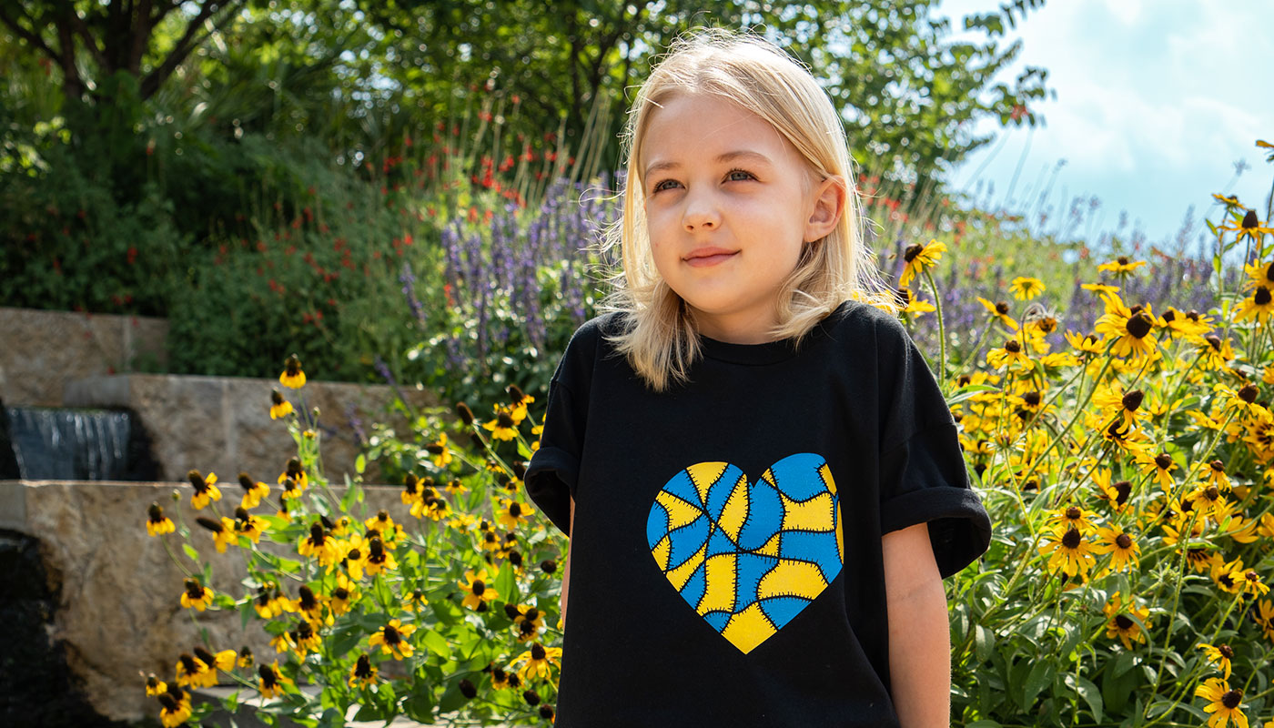 Girl sitting in front of yellow flowers wearing Heart shirt design